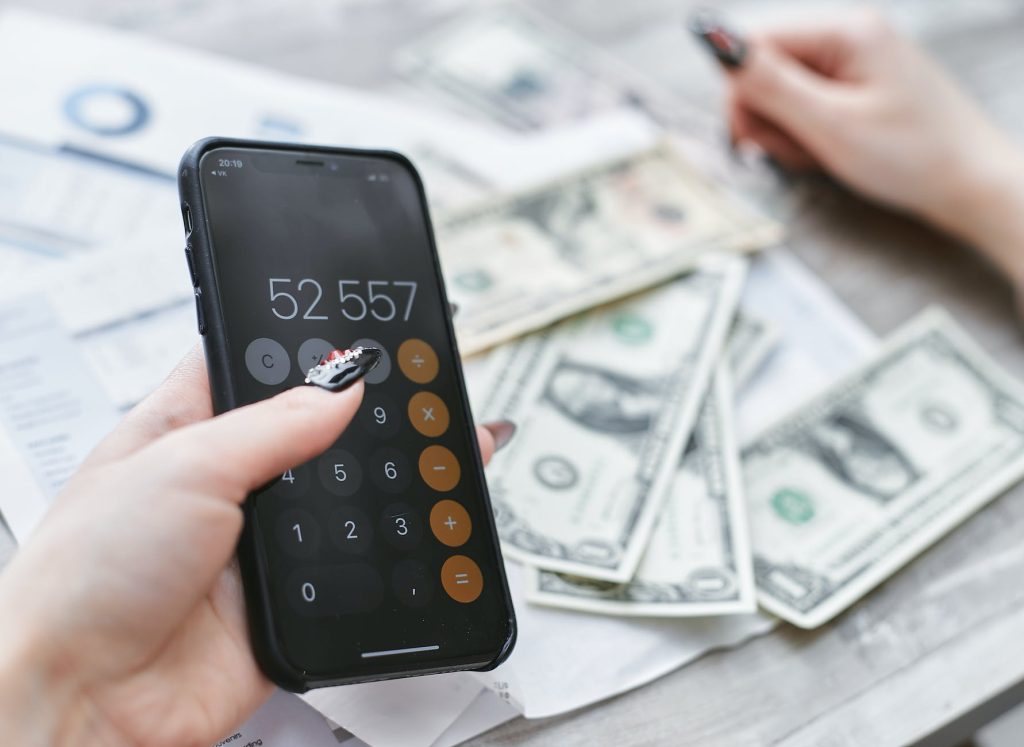 Pessoa usando calculadora do celular; notas de dinheiro